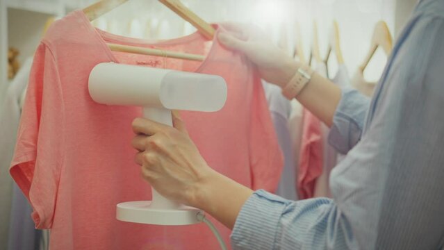 Following modern clothing care technologies, a worker at a European boutique uses a hand-held steamer to steam clothes, smoothing out the fabric and giving it a marketable appearance