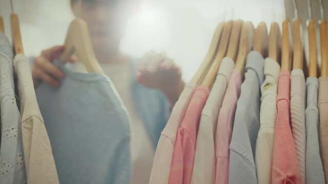 In her home wardrobe, a stylish white housewife chooses clothes based on current trends. She carefully inspects the outfits hanging on hangers to create a fashionable look