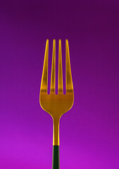 Fork with gold prongs on a purple background
