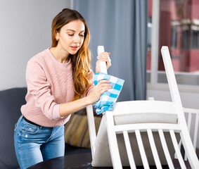 Young european woman cleaning up the apartment wipes a chair with a damp cloth