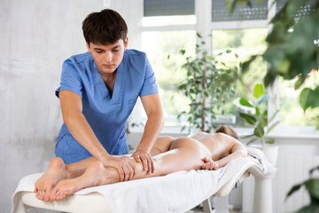 Skilled male physiotherapist conducting leg massage procedure for young woman in therapy room