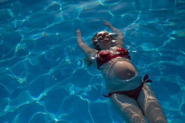 Top view of pregnant woman floating in pool in red bikini. 