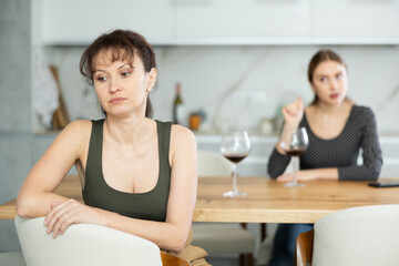 Offended middle-aged woman sitting in the kitchen while other woman talking angrily to her