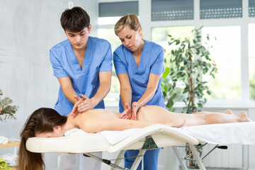 Obraz na płótnie Canvas Young aspiring masseur learning and practicing him techniques under supervision of seasoned female mentor, providing four hands back massage session to woman
