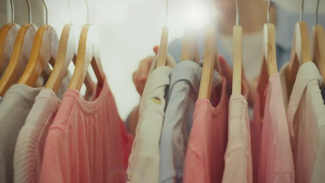 Textile. A trendy European woman dressed in a bright shirt is sorting through clothes on hangers in a fashionable store of stylish things. A young lady considers different options and chooses an image