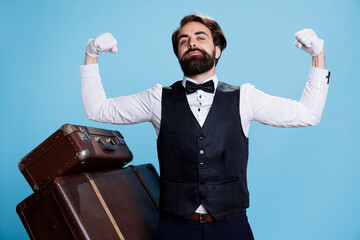 Hotel worker flexing arms in studio, showing off muscles and strength while he wears suit and tie. Classy doorman porter feeling powerful and posing on camera, tourism industry.