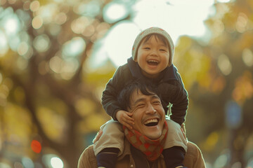 The image portrays a heartwarming moment of a joyful father carrying his happy child on his shoulders, both smiling broadly, set against a blurred autumnal background.
