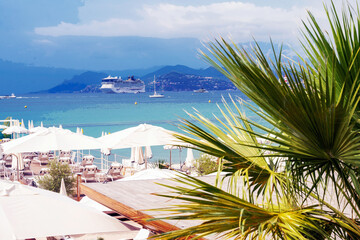 Beach in Cannes (French Riviera) with sun loungers and umbrellas, small palm trees and white...