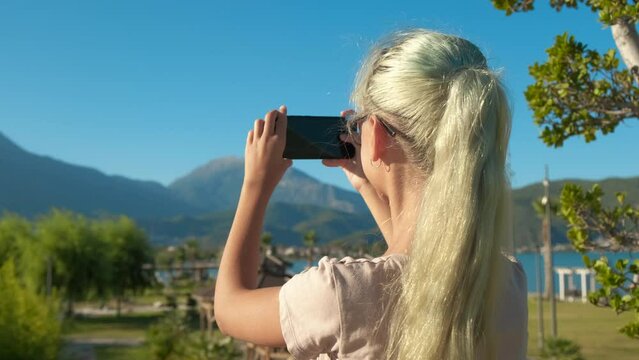 Teen make picture on beach. A view of modern teen girl takes photo on the green sunny beach during summer holidays.