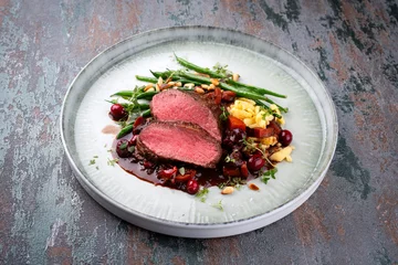 Fototapeten Traditionally roasted saddle of venison fillet with spaetzle, beans and pine nuts in game sauce served as close-up on a Nordic Design plate © HLPhoto