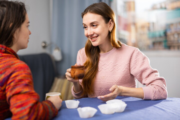 Portrait of young smiling girlfriends having fun together during drinking tea at table at home
