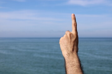 Hand doing,showing number gesture symbol one on blue summer sky nature background. Gesturing number...