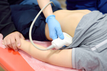 Doctor making abdominal ultrasound for boy using scanner machine. Female doc runs ultrasound sensor...