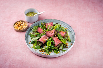 Traditional mixed salad with spinach filled roast beef rolls and pine nuts served as a close-up on a design plate with text space