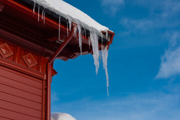 Long dangerous icicles hanging from a roof of a red wooden house. Typical house from a norway...