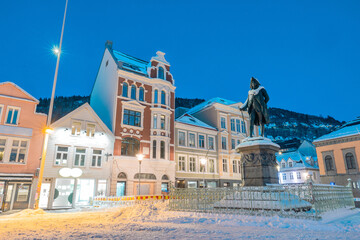 Square in bergen ar night, statue and houses covered in snow and ice. Colorful houses aroud lit by...