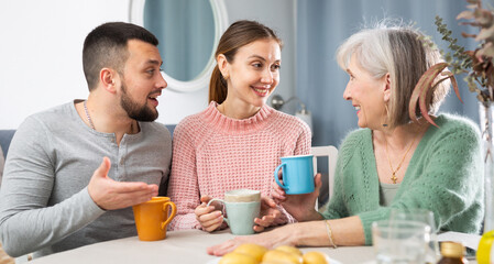 Fototapeta na wymiar Cheerful elderly mother having good time with adult children drinking tea in live room