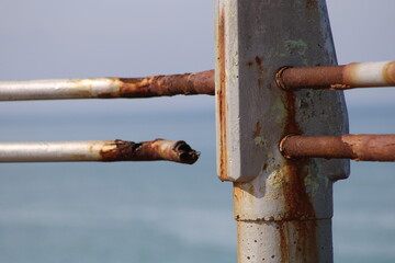A rusty fence with a blue sea in the background.Rusty iron railing, beautiful sea and sky landscape view between rusty railing gap.