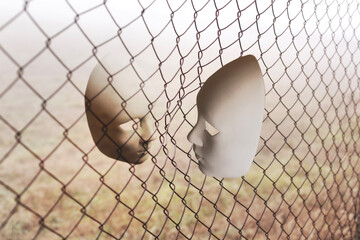 surreal face to face between two masks divided by a metallic net, abstract concept - 739588939