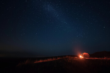 Illuminated camping tent with campfire under sky full of stars. Night time tranquility and calm. Concept of wilderness camping and solitude 