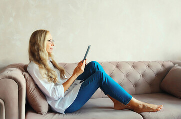 Middle-aged woman working with digital tablet computer sitting on sofa at home