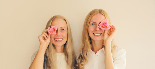 Happy two women, mother and adult daughter covering her eyes with pink rose flower buds