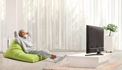 African american guy sitting on a green bean bag armchair and watching tv