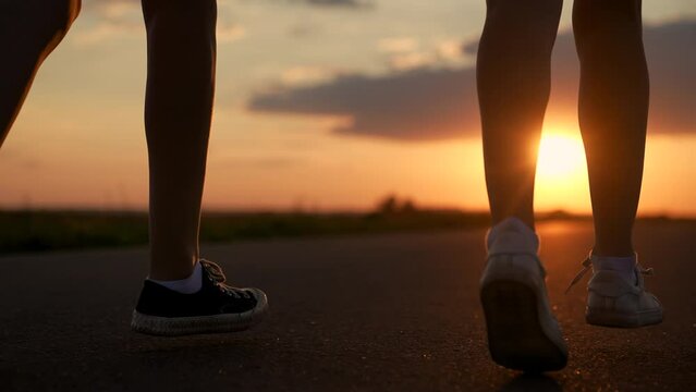 Girls feet run along road training, , teamwork of running athletes. Slow motion. Athletic young women running along an asphalt road at sunset, healthy fitness lifestyle. People run in sun together
