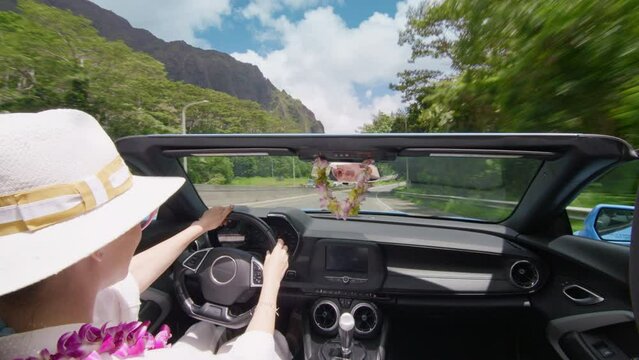 Woman travels by Oahu island 4K. Happy tourist in blue convertible car driving by H3 highwayUSA. Scenic Hawaii landscape seen from cabriolet open car. Elegant woman in lei flowers enjoying epic views