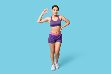 Fototapeta na wymiar Young woman in sportswear showing OK on blue background