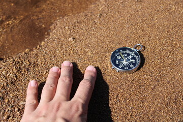 Direction compass and male hand on the sand at the beach. help themed photo