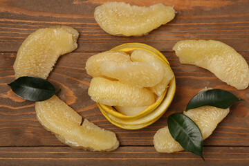 Sweet pomelo pieces with peel and leaves on wooden background