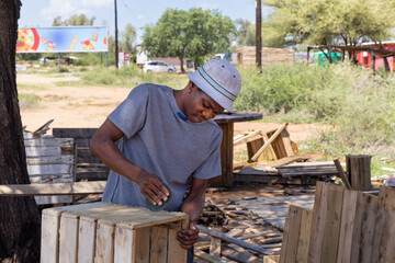 african american carpenter making a wendy house, wooden shed outdoors, close up, he is grinding the planks and assemble them in panels