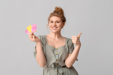 Beautiful young woman with credit cards showing thumb-up gesture on grey background