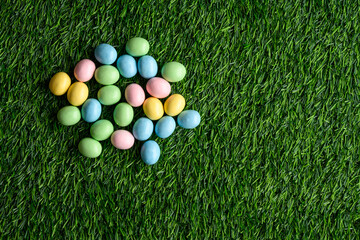 Naklejka premium Happy Easter, pastel colored candy coated Easter eggs on artificial green grass 