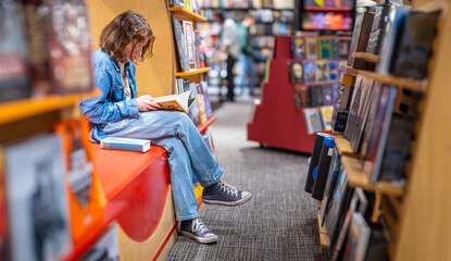 Teenage girl reading the book in large bookshop of London