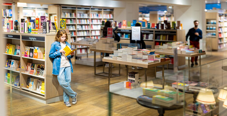 Teenage girl reading the book in large bookshop of London