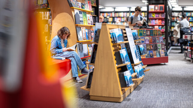 Teenage girl reading the book in large bookshop of London
