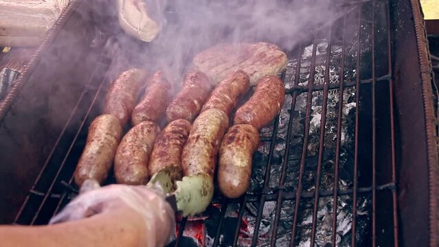 Polish sausages being grilled on a barbecue with smoke and flames visible