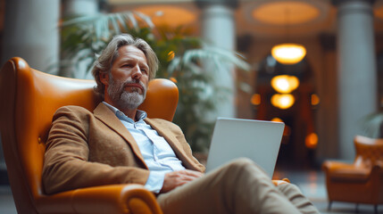 Mature businessman sitting in an office lobby with a laptop. Male executive working in the office...