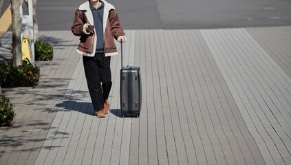 冬の昼の街でスーツケースを持って歩く一人の若者の姿