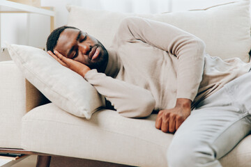 Stressed African American man with a painful headache sitting alone on the couch at home The image...