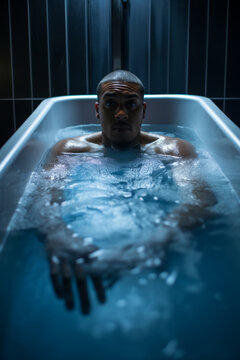 Black young athlete taking a cold plunge in a bathtub after practice