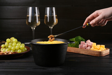 Woman dipping walnut into fondue pot with melted cheese at black wooden table, closeup