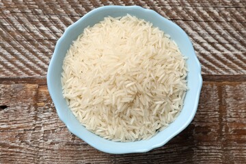 Raw basmati rice in bowl on wooden table, top view