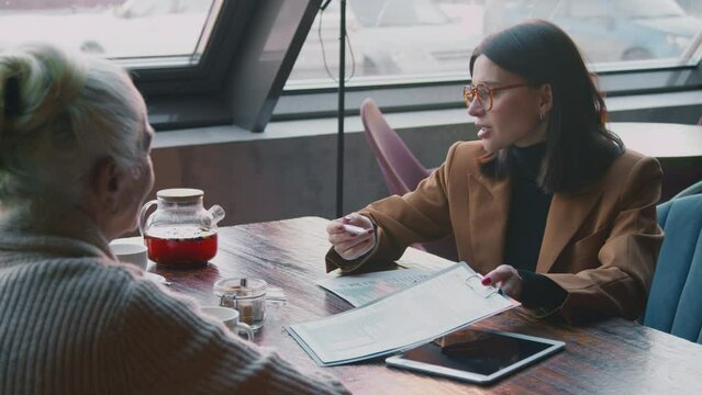 Medium shot of Caucasian female financial consultant having personal meeting with elderly couple in cafe, presenting insurance policy, explaining details of transactions, old lady listening, nodding