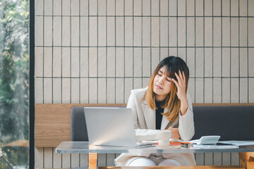 Stressed businesswoman at a cafe with laptop, showing signs of fatigue or headache during a busy workday.