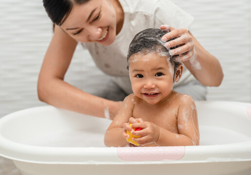 mother bathing and washing her infant baby hair with shampoo while playing a rubber duck toy in bathtub