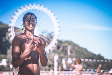 17-year-old afro-descendant teenager with braids in hair and no shirt, various facial expressions, lifestyle concept, ferris wheel of Camboriu resort in the background - obrazy, fototapety, plakaty