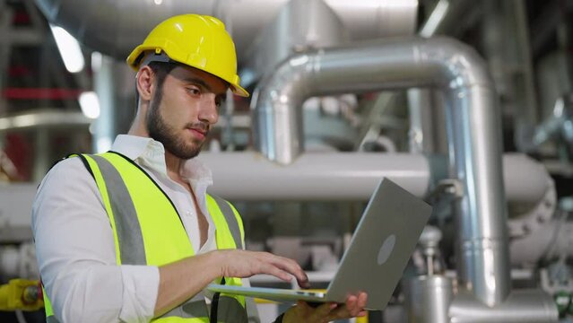 Professional male electrical engineer working on laptop computer at factory site control room. Industrial technician worker maintenance and checking power system at manufacturing plant room.